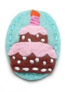 Süße, aus Filz-Material gefertigte Haarspange im Motiv Birthday Cake Blue. Das Motiv zeigt eine braune Geburtstagstorte mit pinkfarbenen Elementen auf hellblauem Grund.